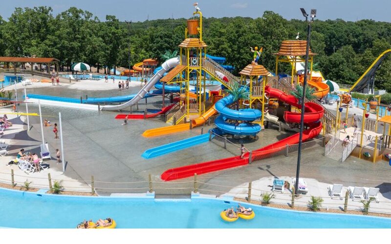 Full Adventure Island play structure with thatched towers, slides, and the lazy river curving in the foreground