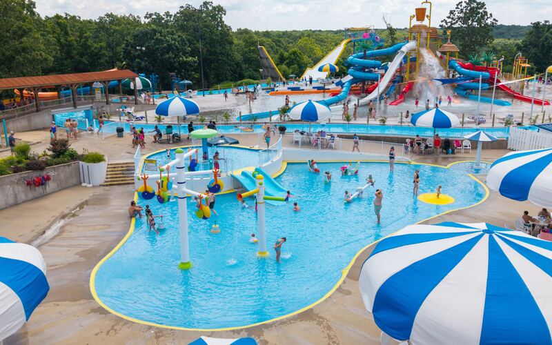 Aerial view of the kiddie splash pad with colorful play structures, shallow water, and blue and white umbrellas