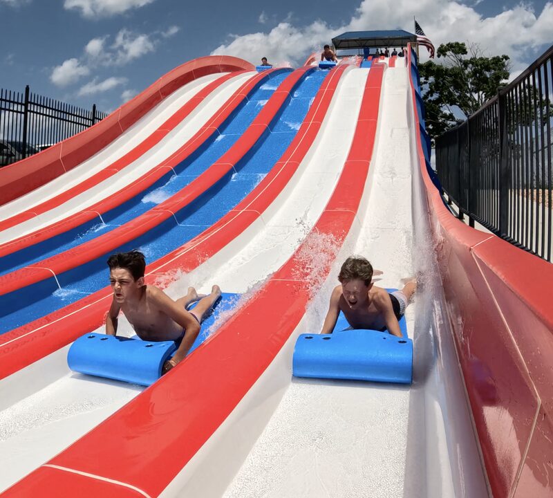 Two riders racing on blue mats down the red, white, and blue lanes of Patriot's Plunge